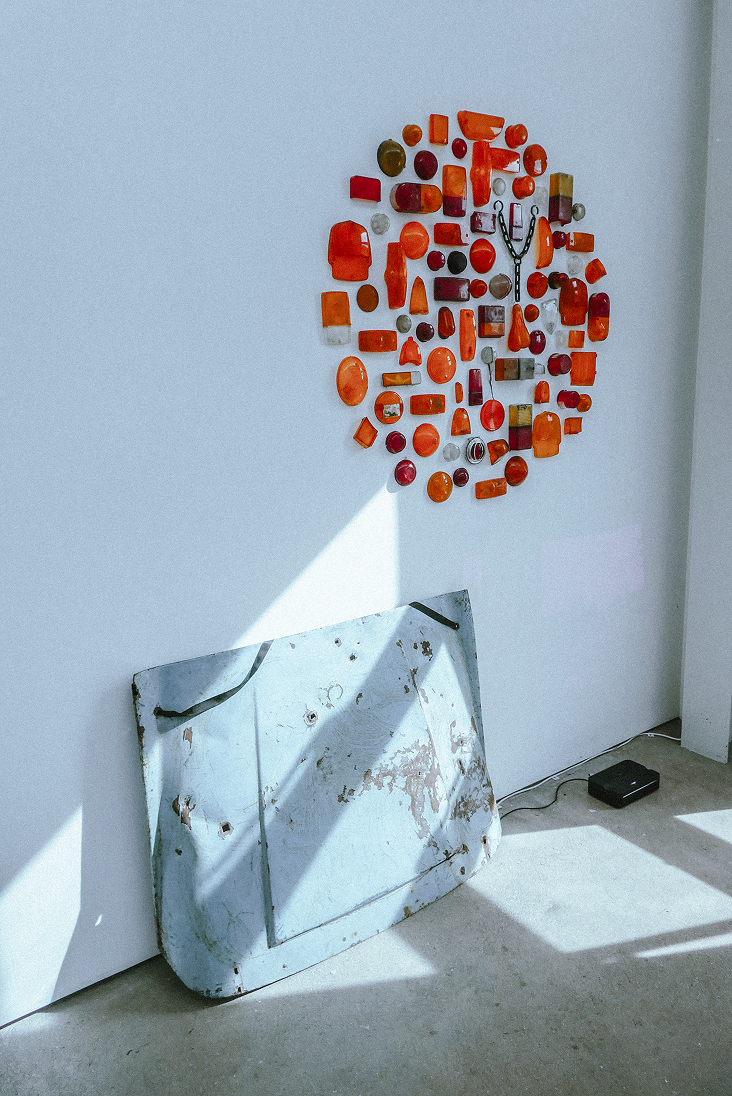Installation view of amber and red automotive lenses mounted above a weathered bonnet panel