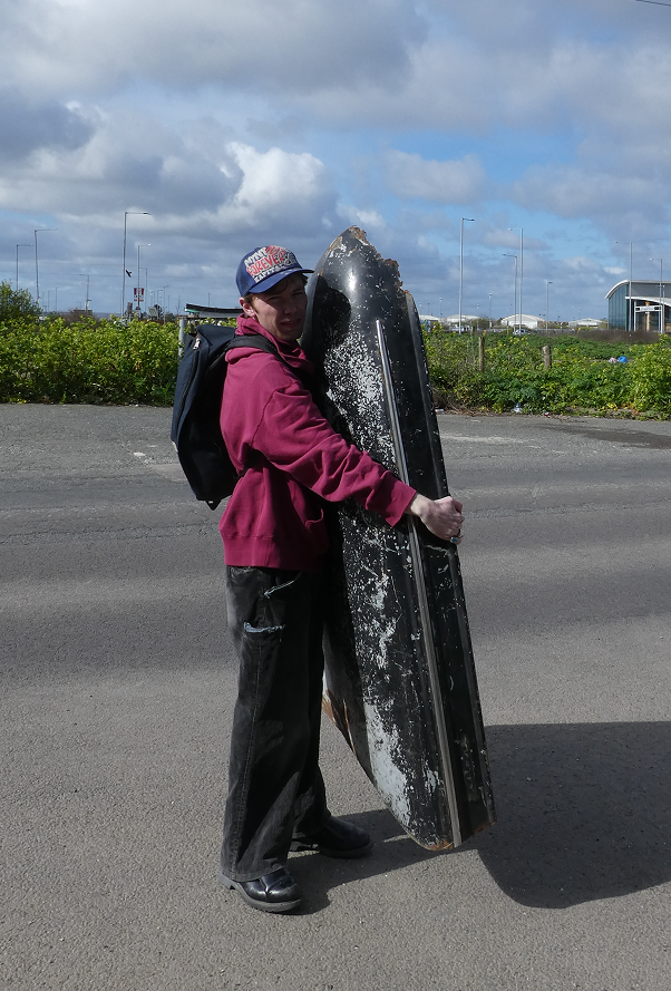 Colin carrying a large weathered black car bonnet on the Isle of Sheppey